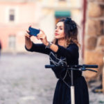 Happy girl taking selfie with camera while riding a kick scooter